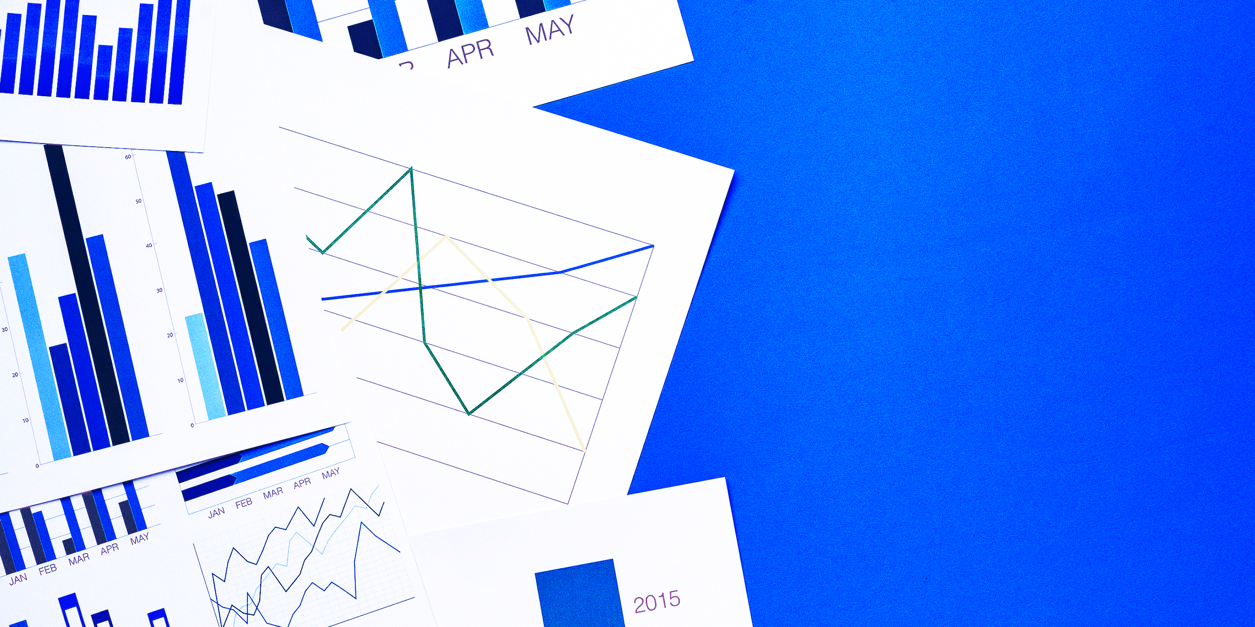 a stack of papers with graphs and charts on a blue background. The text on the papers is "APR", "MAY", "JAN FEB MAR APR MAY", and "2015".